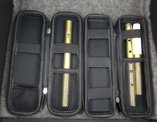 Travel cases with whistles inserted.  The cases are black with zips around the outside, and the whistles are secured by elastic straps and mesh pockets.