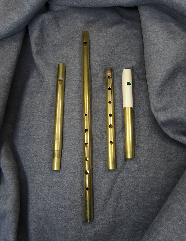 Three MackBeth brass whistles resting on grey felt.  From left to right, they are the telescoping, traditional, and two-piece models.